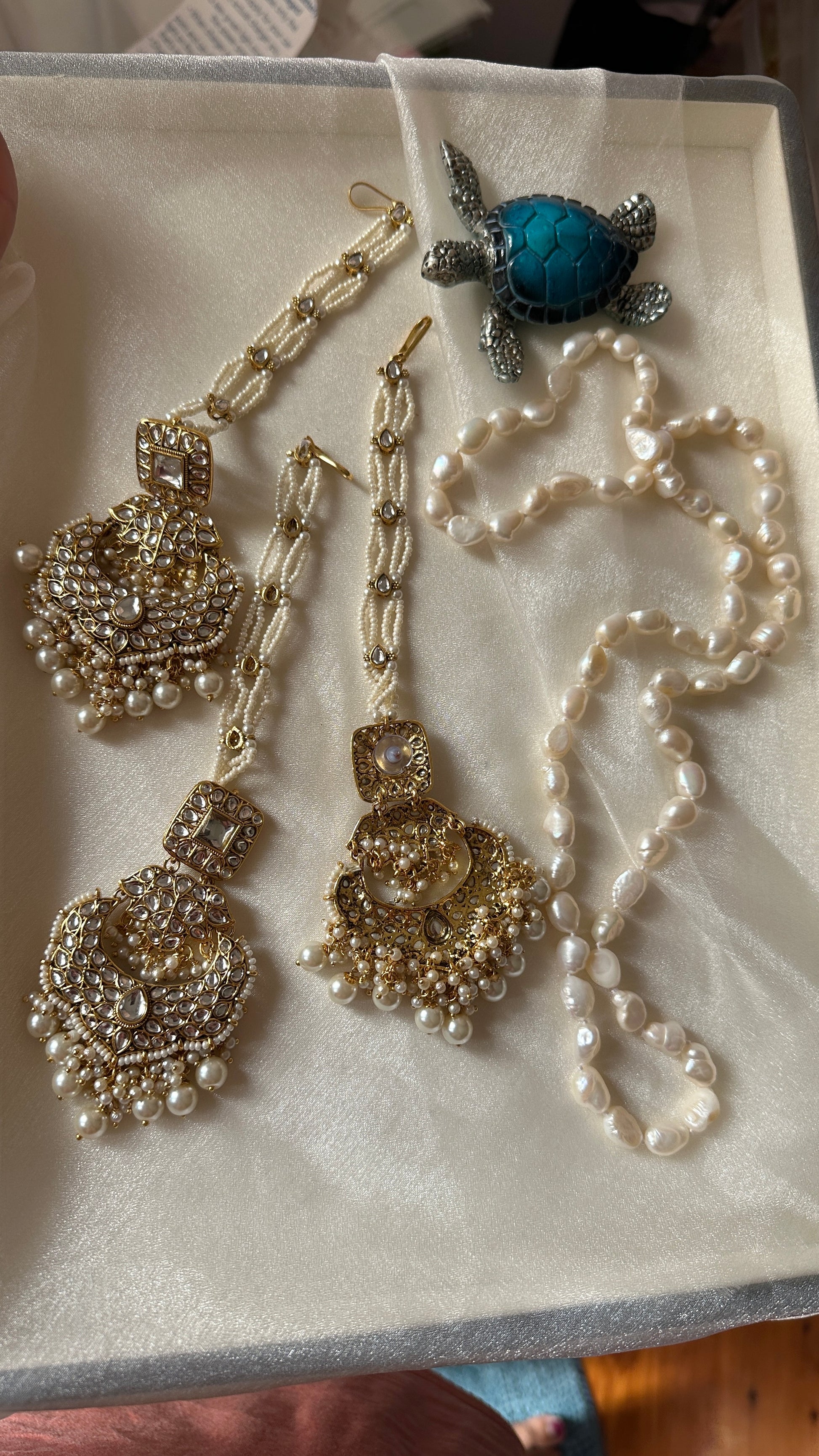 A collection of golden kundan earrings and tikka with intricate designs, featuring pearls and predominantly gold colors.