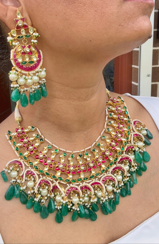 Close-up of a person wearing an ornate necklace and earrings with green, pink, and gold colors.
